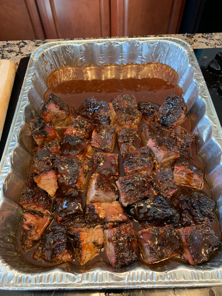 Burnt ends soaking in broth, coated with sauce
